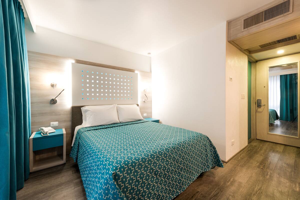 Una habitación de hotel con cama, mesita de noche, espejo y puerta.