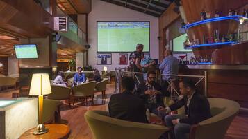 A bar area with a large screen displaying a sports game, seating arrangements, and a bar counter with bottles.