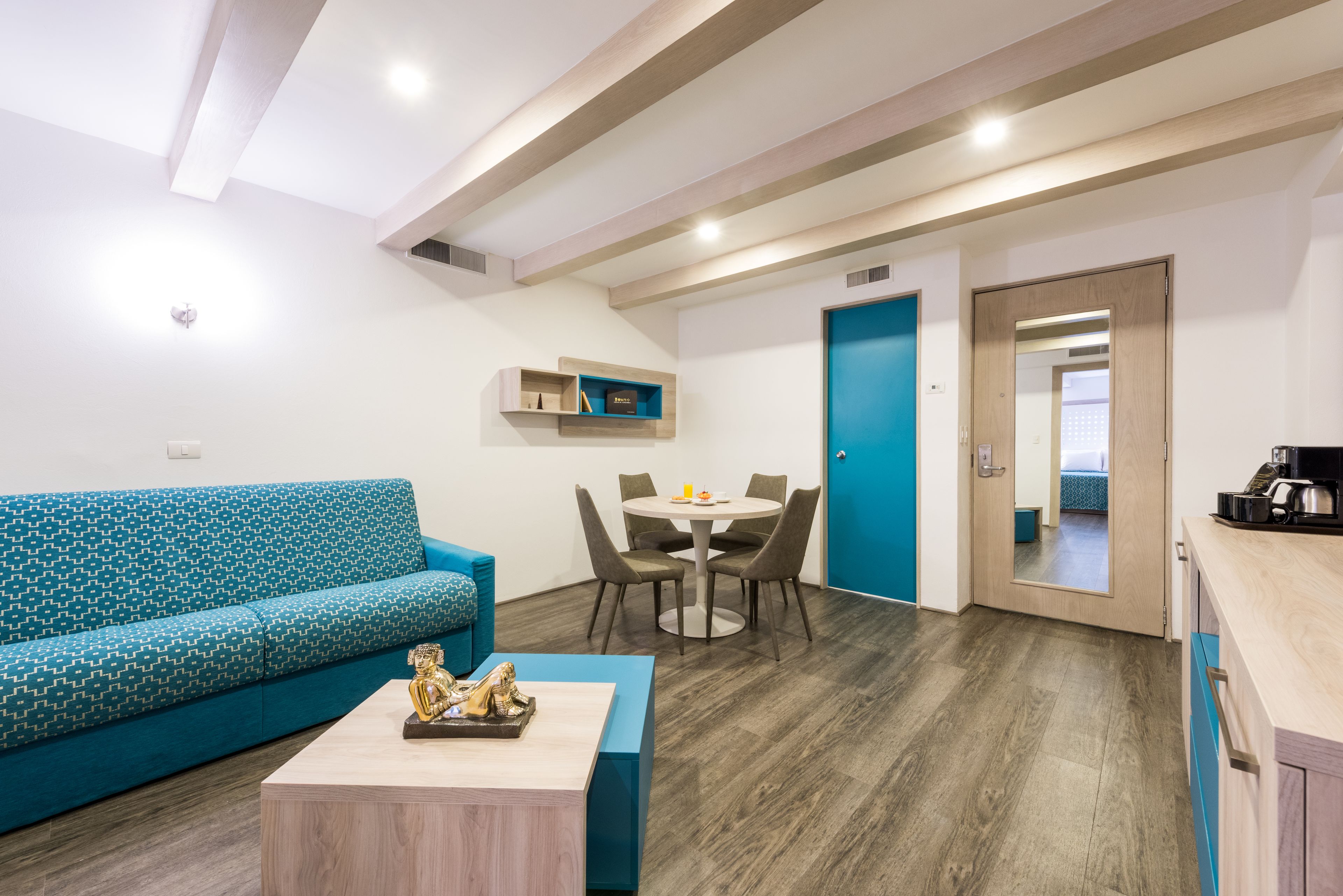 A modern living room with a teal sofa, a coffee table, and a dining area with a small table and chairs.