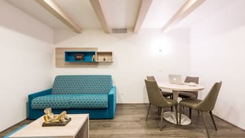 A modern living room with a teal sofa, a coffee table, and a dining area with a round table and chairs.