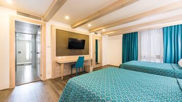 Habitación de hotel con techo de madera, un escritorio con silla, cama con ropa de cama estampada y televisor montado en la pared.