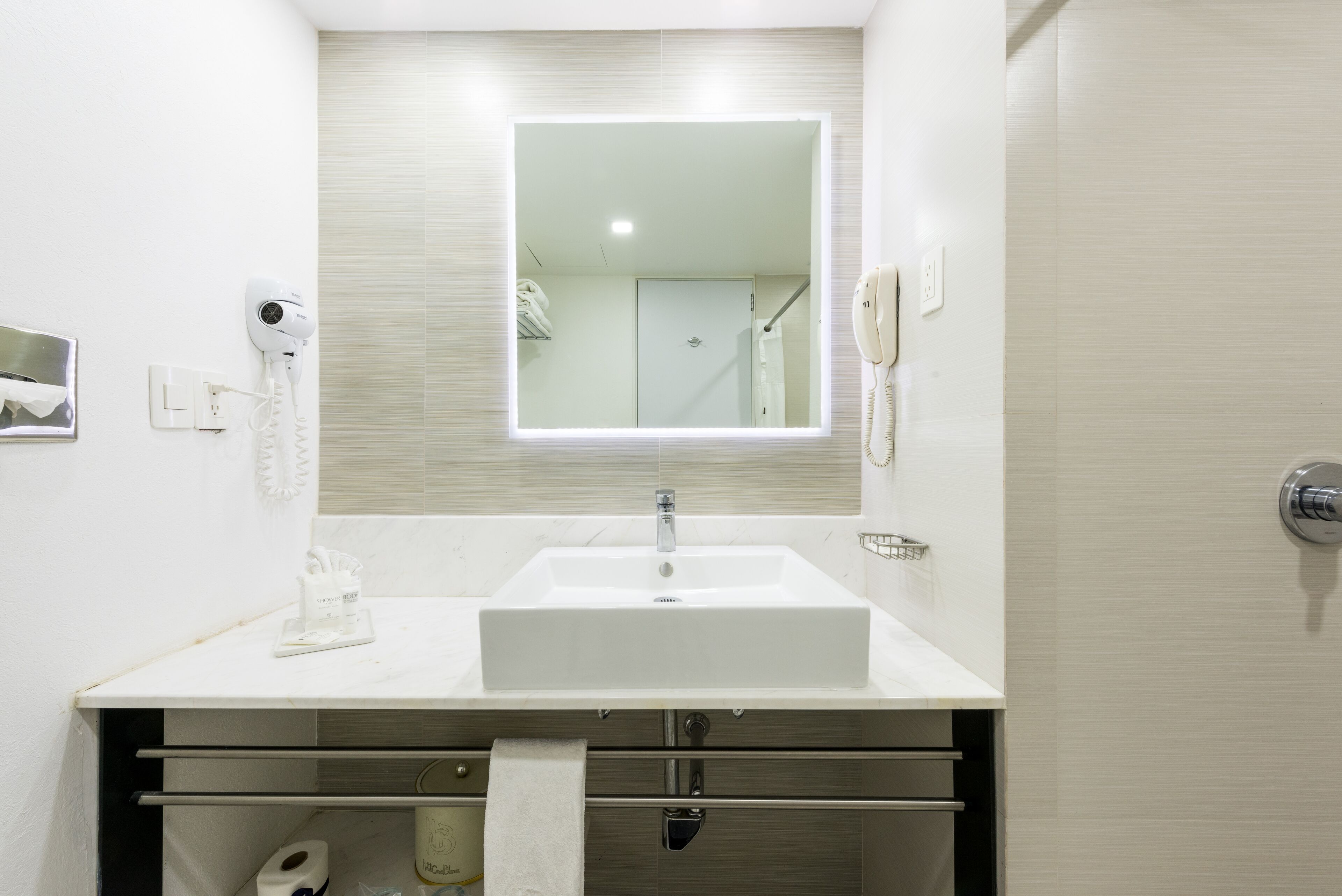 A bathroom with a white sink, a mirror, a hairdryer, a phone, and a towel rack.
