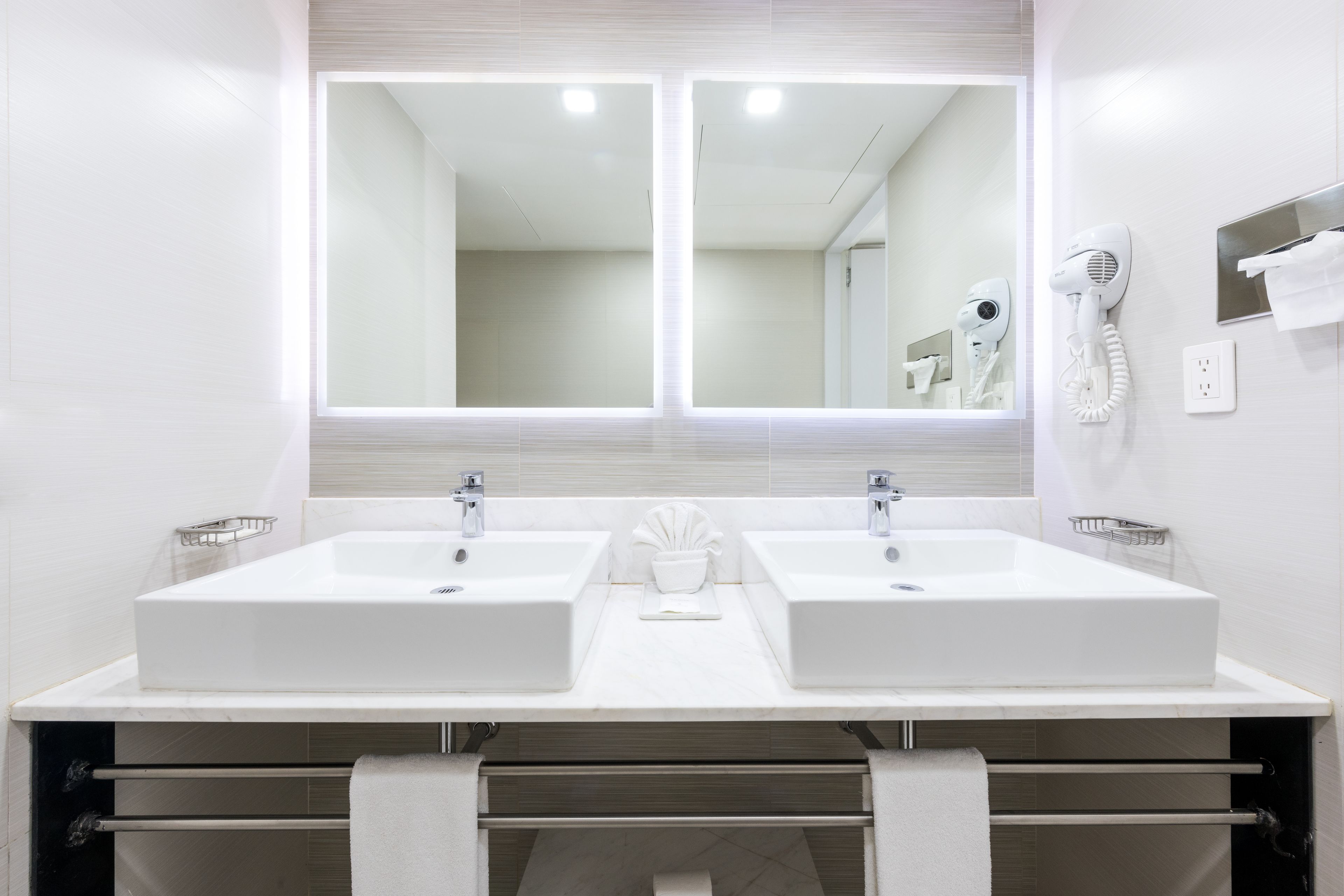 A modern bathroom with two sinks, a large mirror, and a hairdryer on the wall.