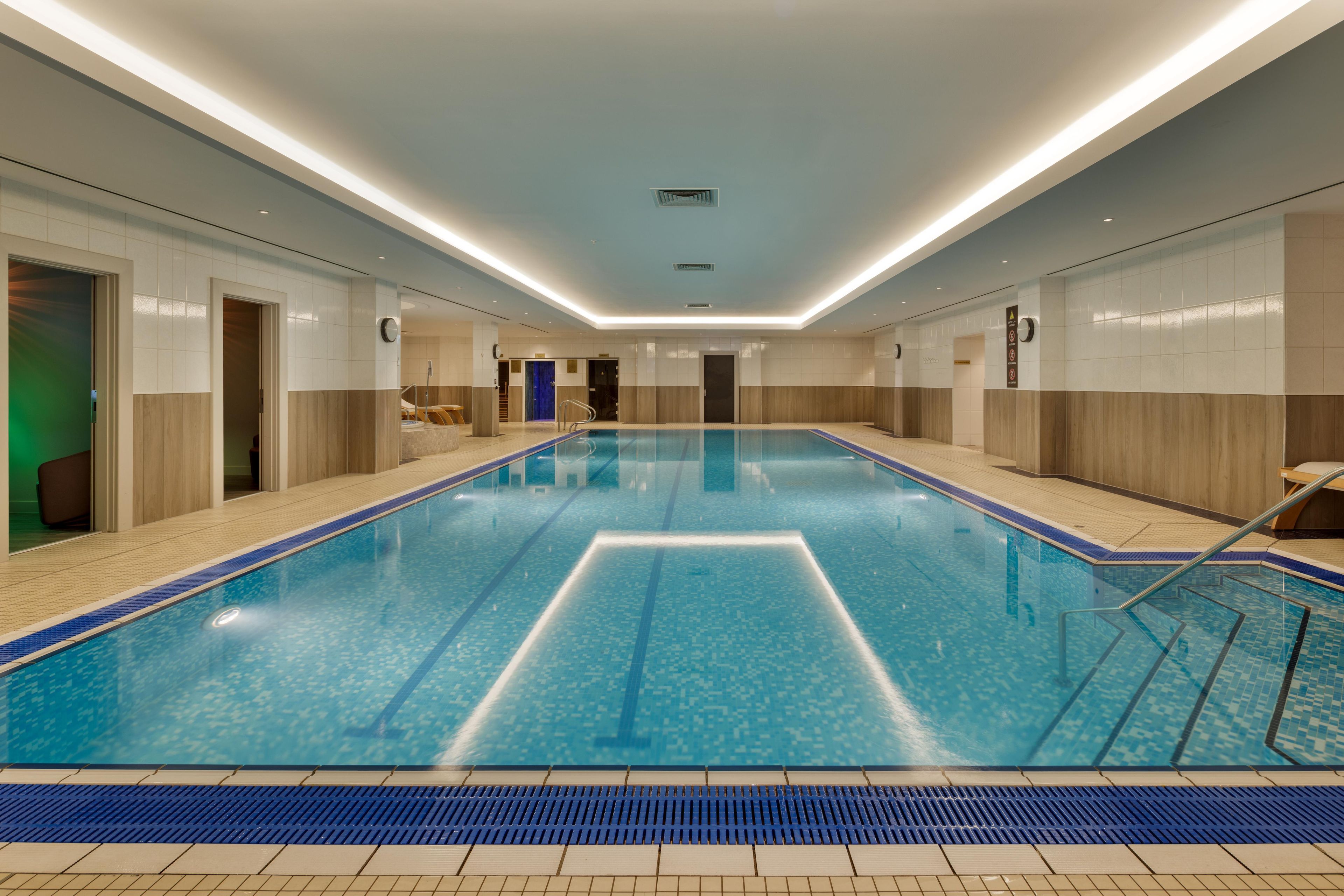 Una amplia piscina interior con agua cristalina y paredes de azulejos, sobre un suelo de madera.
