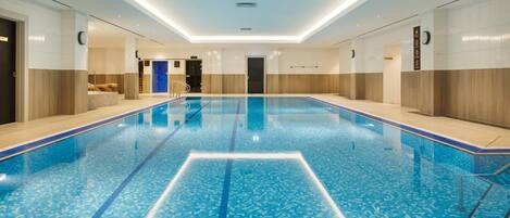 Una amplia piscina interior con agua cristalina azul, rodeada de paneles de madera y un diseño moderno en el techo.
