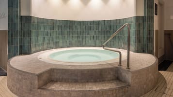 Un jacuzzi circular con una escalera metálica, rodeado de piso y paredes de azulejos.