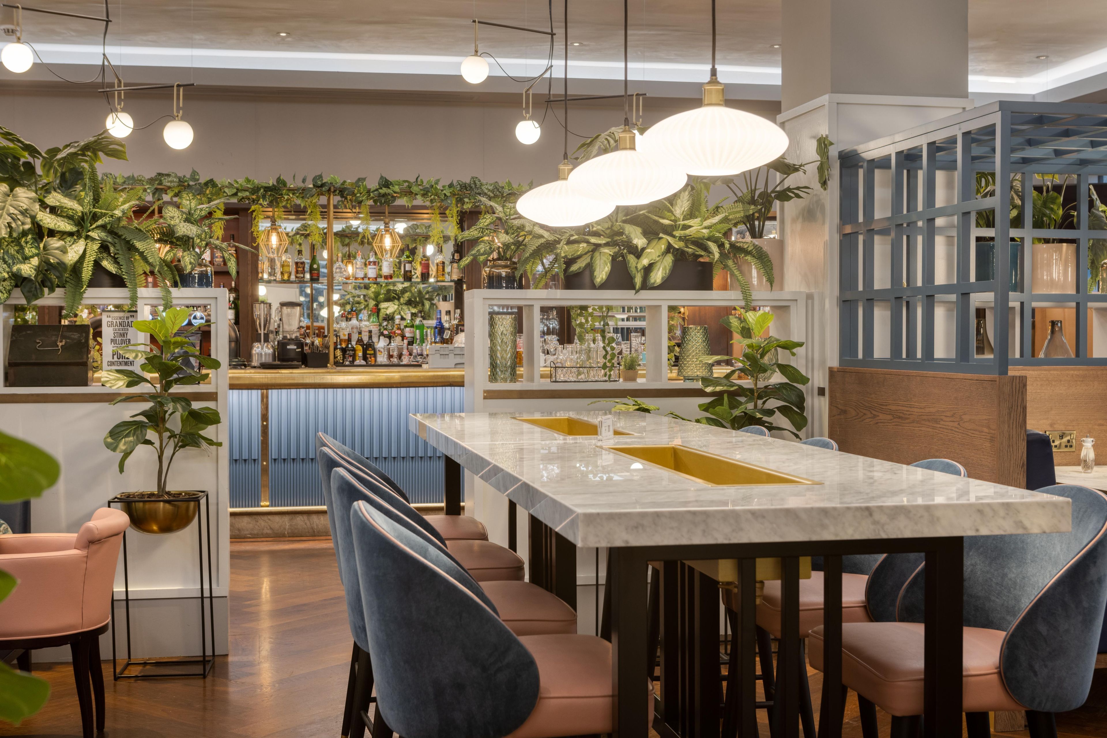 Een bar met een marmeren toonbank, zitplaatsen en hangplanten.