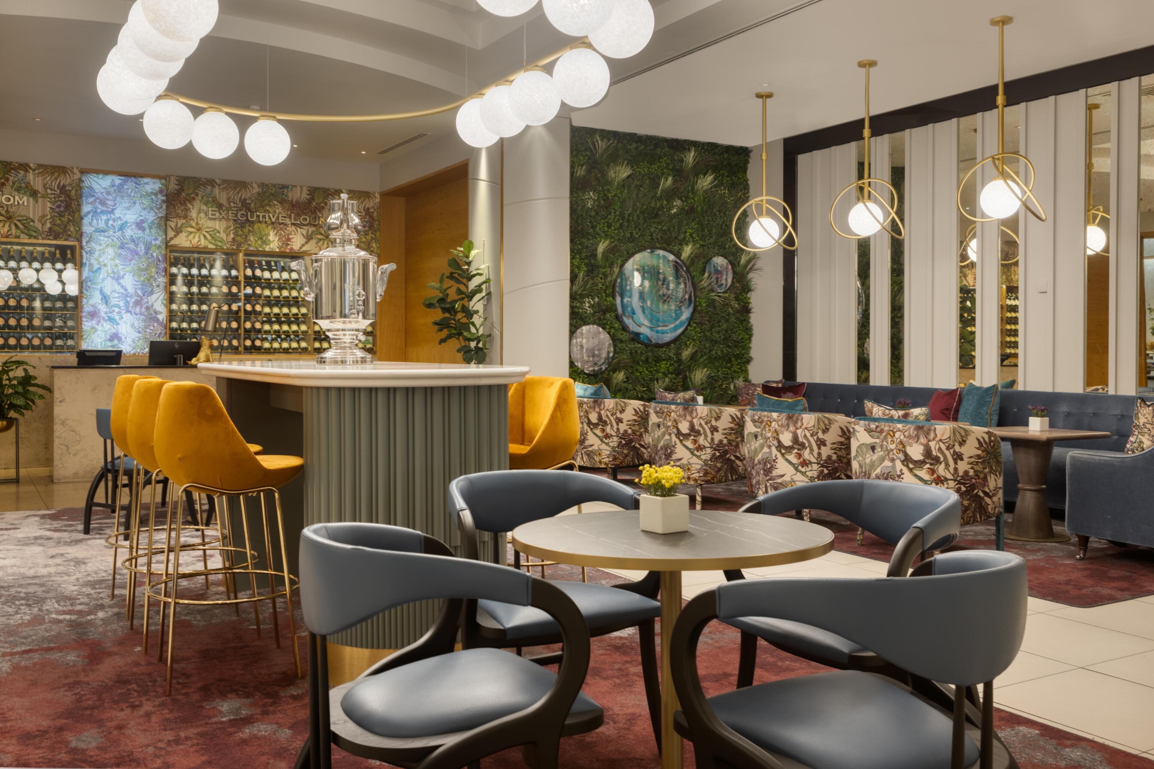 Un área de bar moderna con barra, asientos con sillas y sofás, y decoración en la pared.