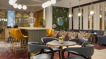 Un área de bar moderna con barra, asientos con sillas y sofás, y decoración en la pared.