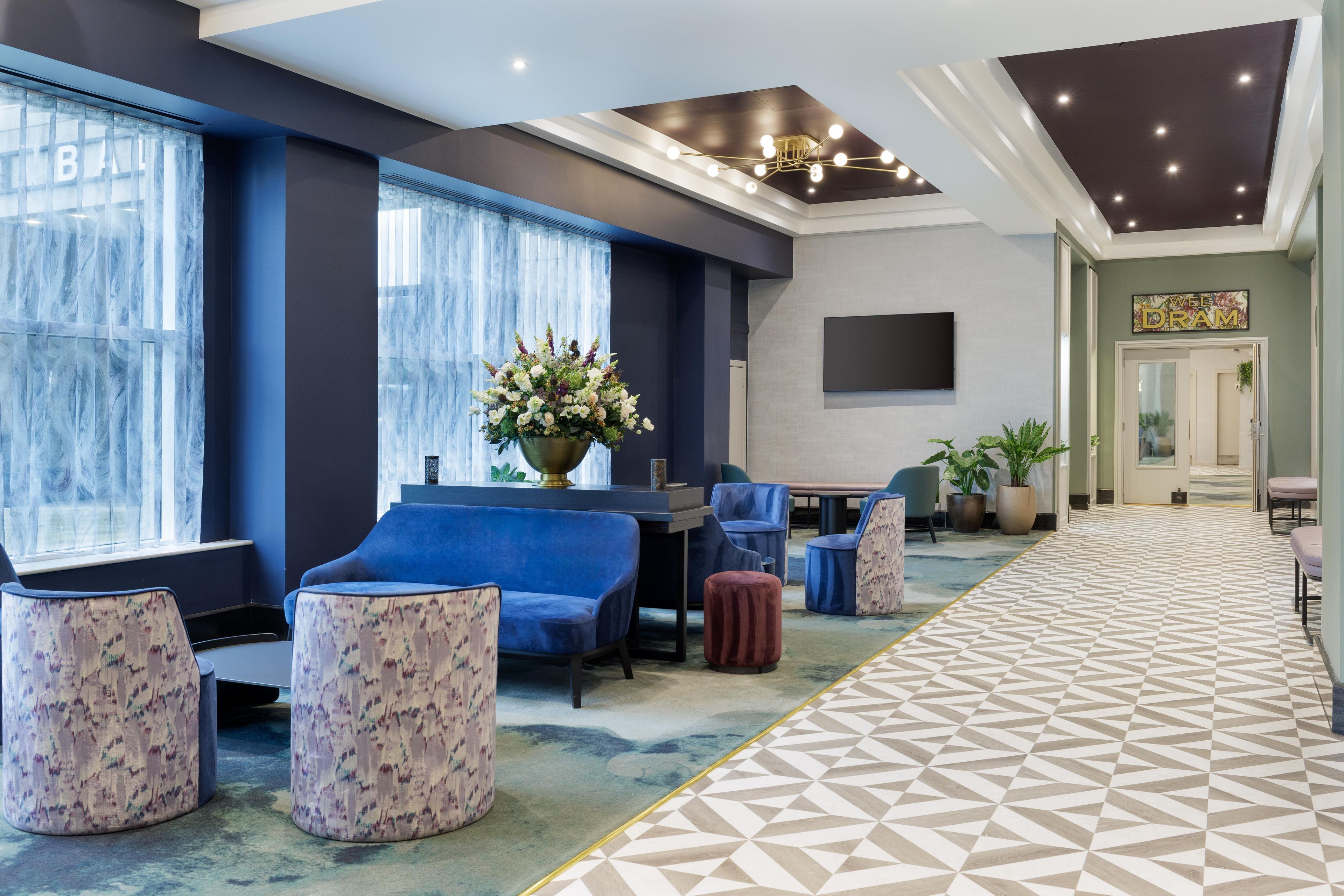 A hotel lobby with a seating area, a large flower arrangement, and a television screen.