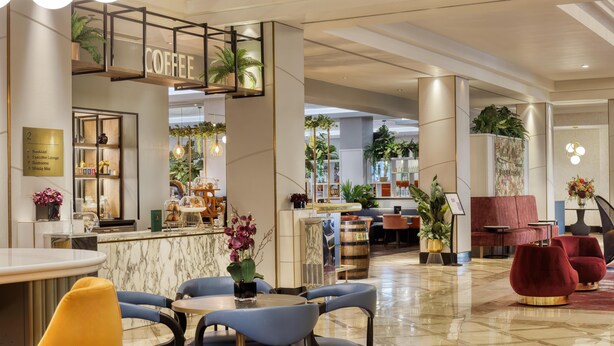 Un moderno vestíbulo de hotel con una barra de café, zonas de estar y una recepción.