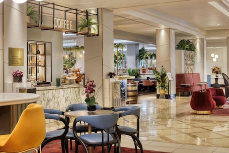 A modern hotel lobby with a coffee bar, seating areas, and a reception desk.