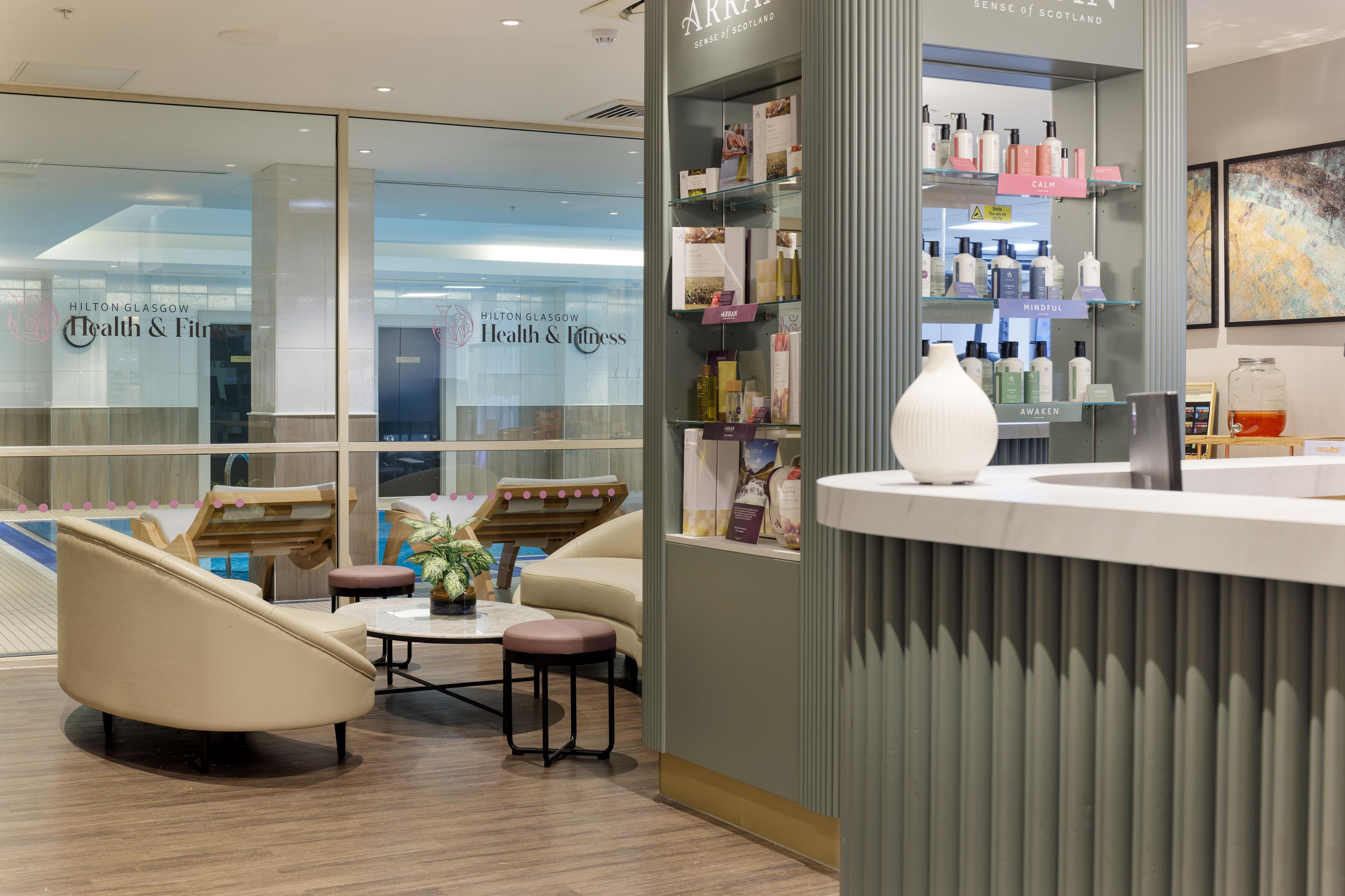 A hotel lobby with a reception desk, seating area with chairs and a table, and a glass wall with the hotel's name.