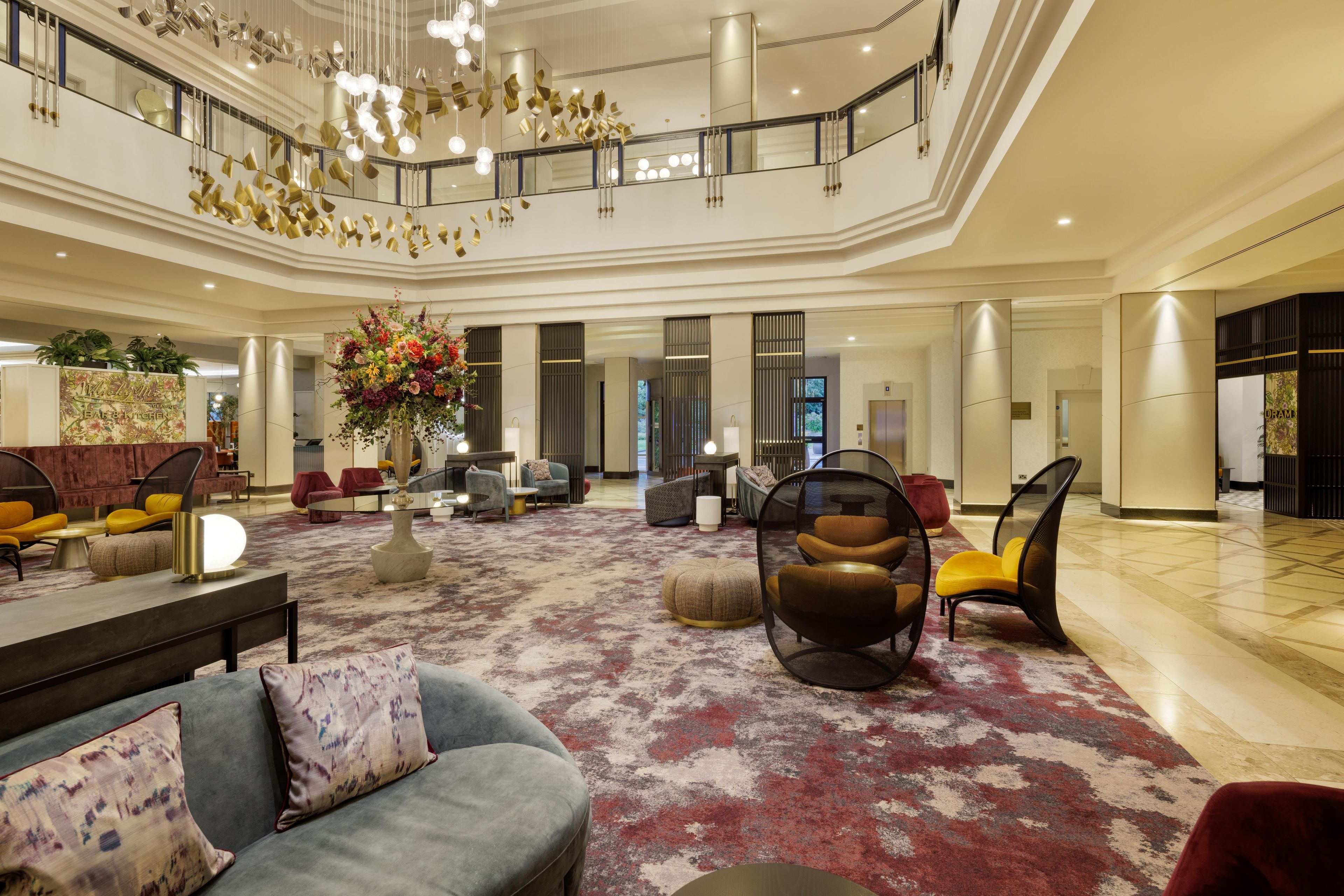 A spacious lobby with a high ceiling, a central floral arrangement, and a variety of seating options including sofas and chairs.