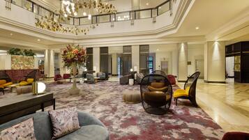 A spacious lobby with a high ceiling, a central floral arrangement, and a variety of seating options including sofas and chairs.