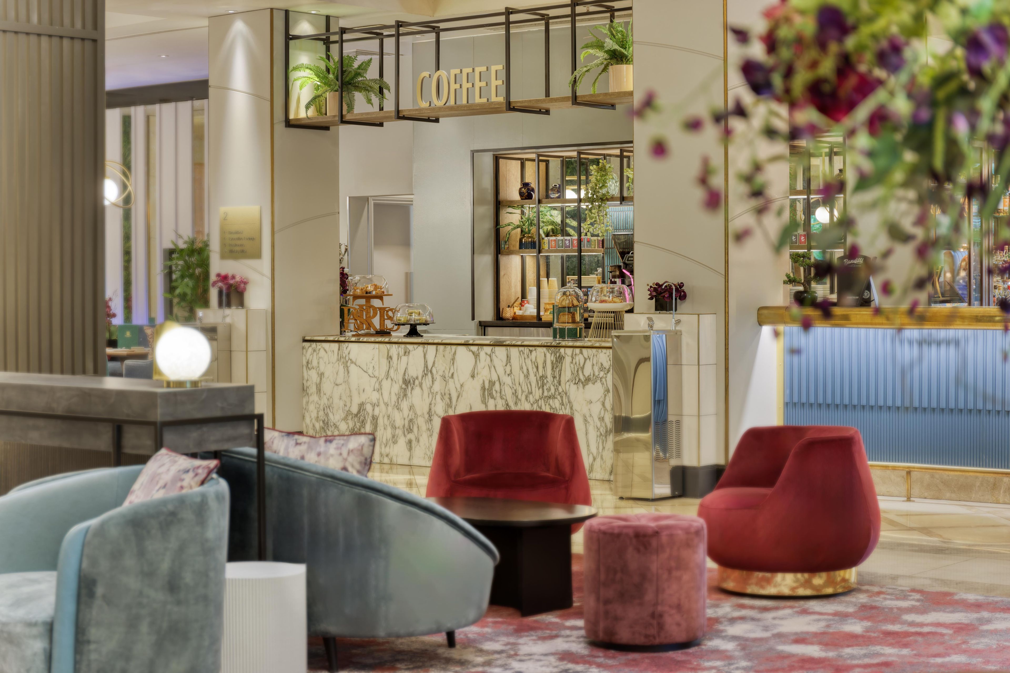 Un moderno vestíbulo de hotel con una barra de café, zona de estar y plantas decorativas.