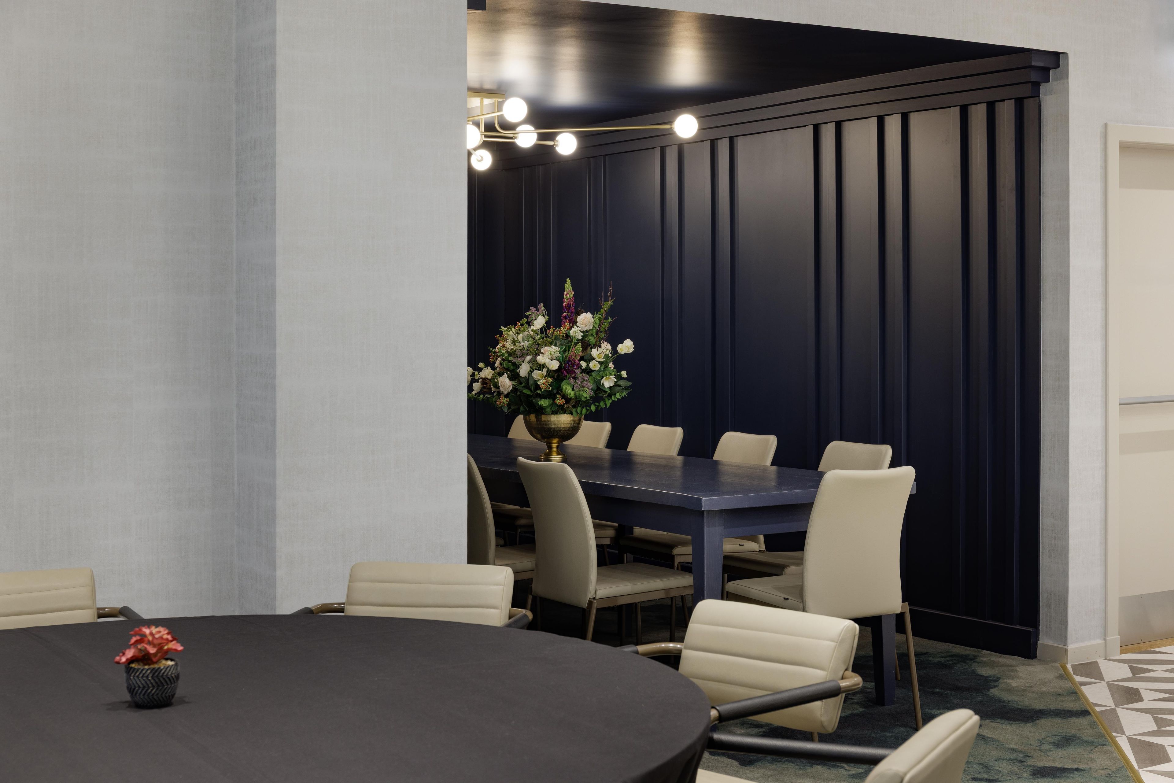 A conference room with a round table, six chairs, and a floral centerpiece.