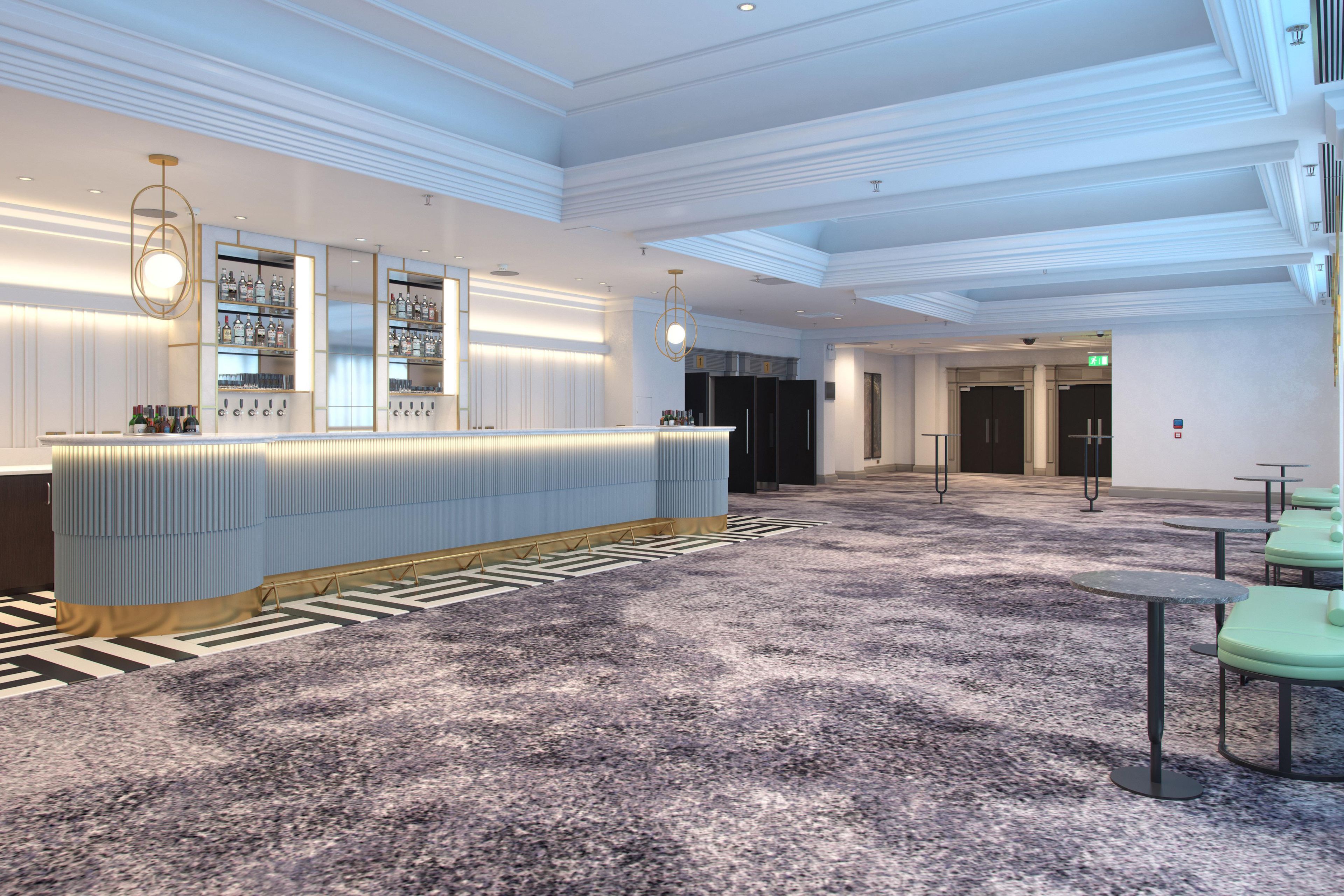 A modern hotel lobby with a reception desk, seating area, and a staircase.