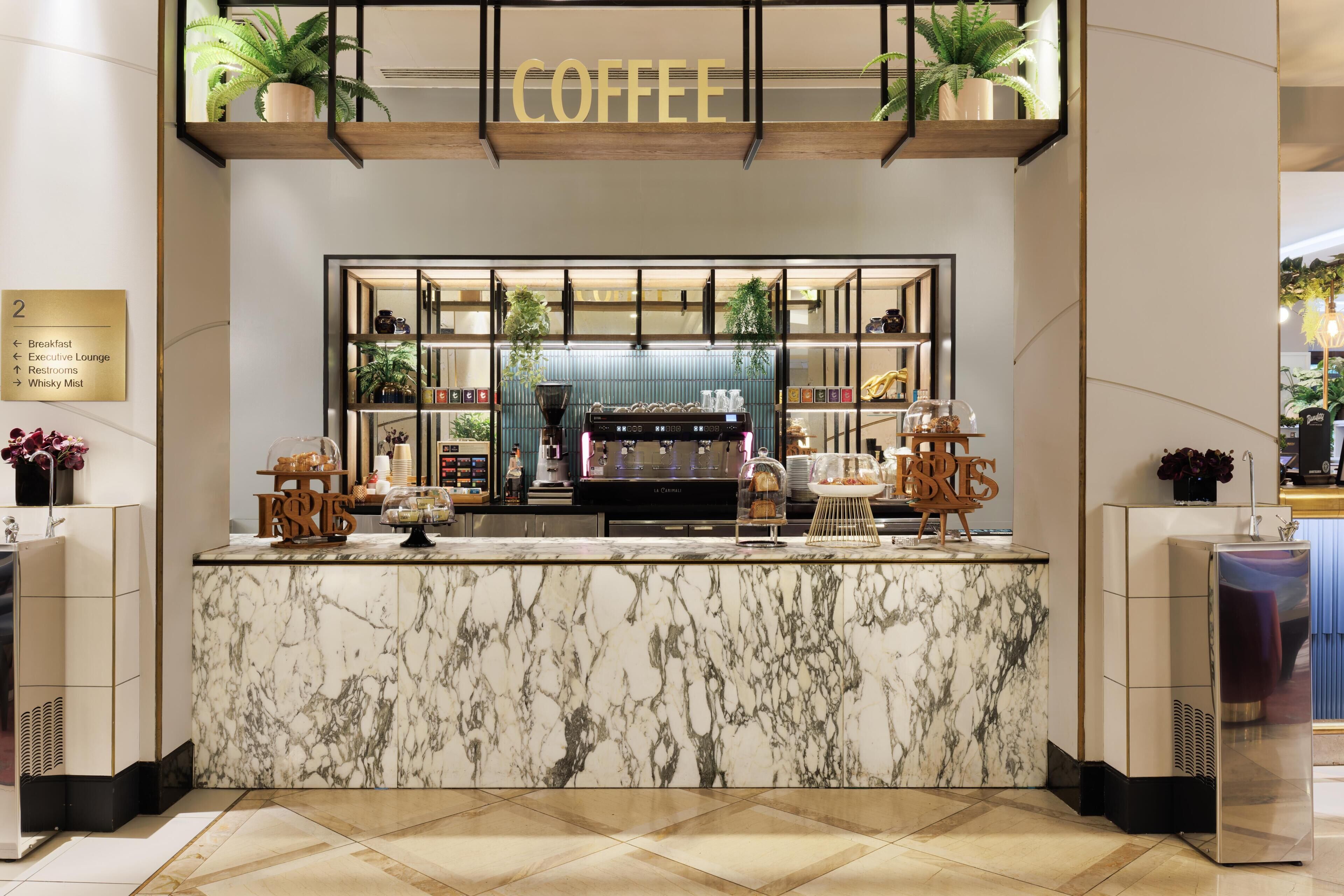 A marble counter with a coffee station, including a coffee machine and various coffee cups.