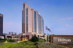 A tall, modern hotel building with a prominent 'Hilton' sign, surrounded by well-maintained greenery and a clear sky. - Hilton Glasgow (Glasgow)