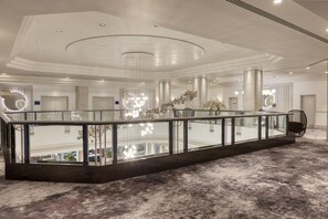 A spacious hotel lobby with a glass railing, a high ceiling with a central light fixture, and a view of the cityscape. - Hilton Glasgow (Glasgow)