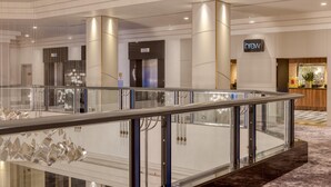 Un moderno vestíbulo de hotel con barandilla de vidrio, una cafetería y un mostrador de recepción.