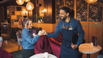 A man and a woman shaking hands in a warmly lit indoor setting with wooden walls and hanging light fixtures.