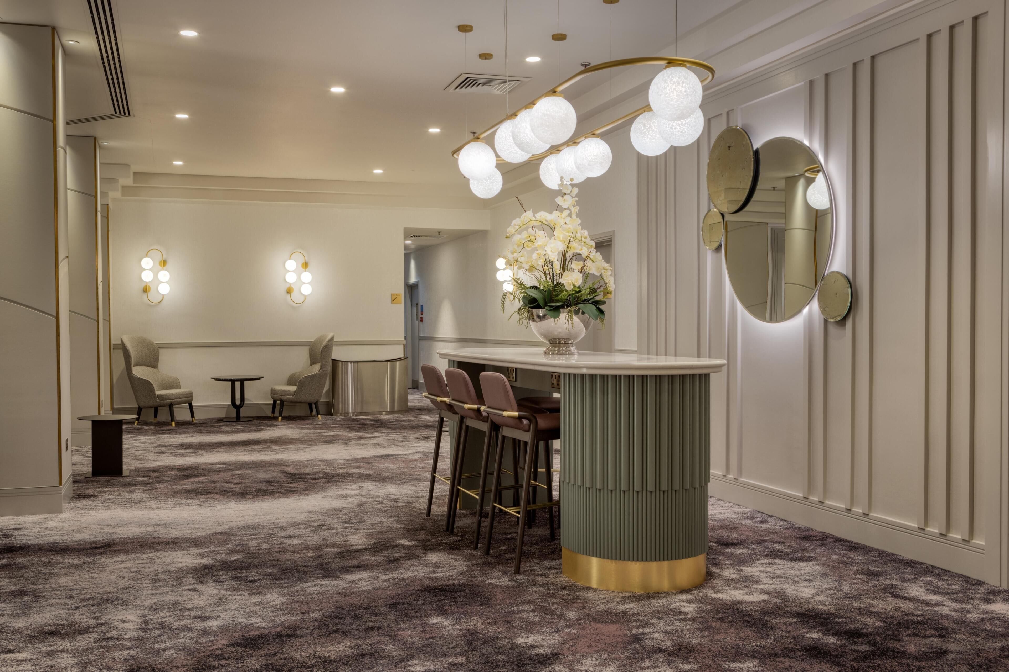 A hotel lobby with a bar area, seating, a decorative mirror, and a floral centerpiece.