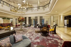 A spacious lobby with a high ceiling, a central floral arrangement, seating areas, and a staircase. - Hilton Glasgow (Glasgow)