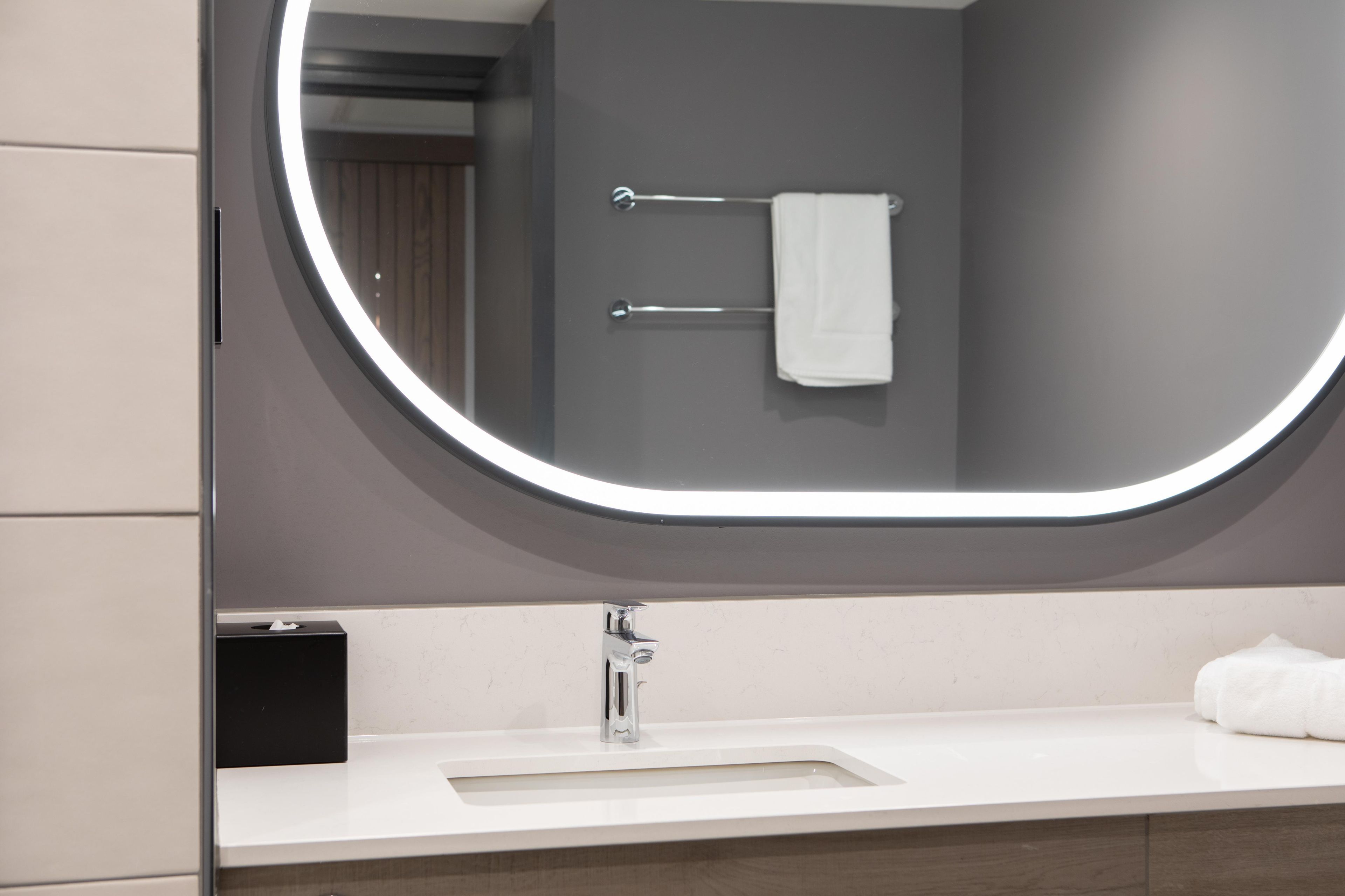 Un baño con un espejo redondo, un lavabo blanco y un perchero para toallas.