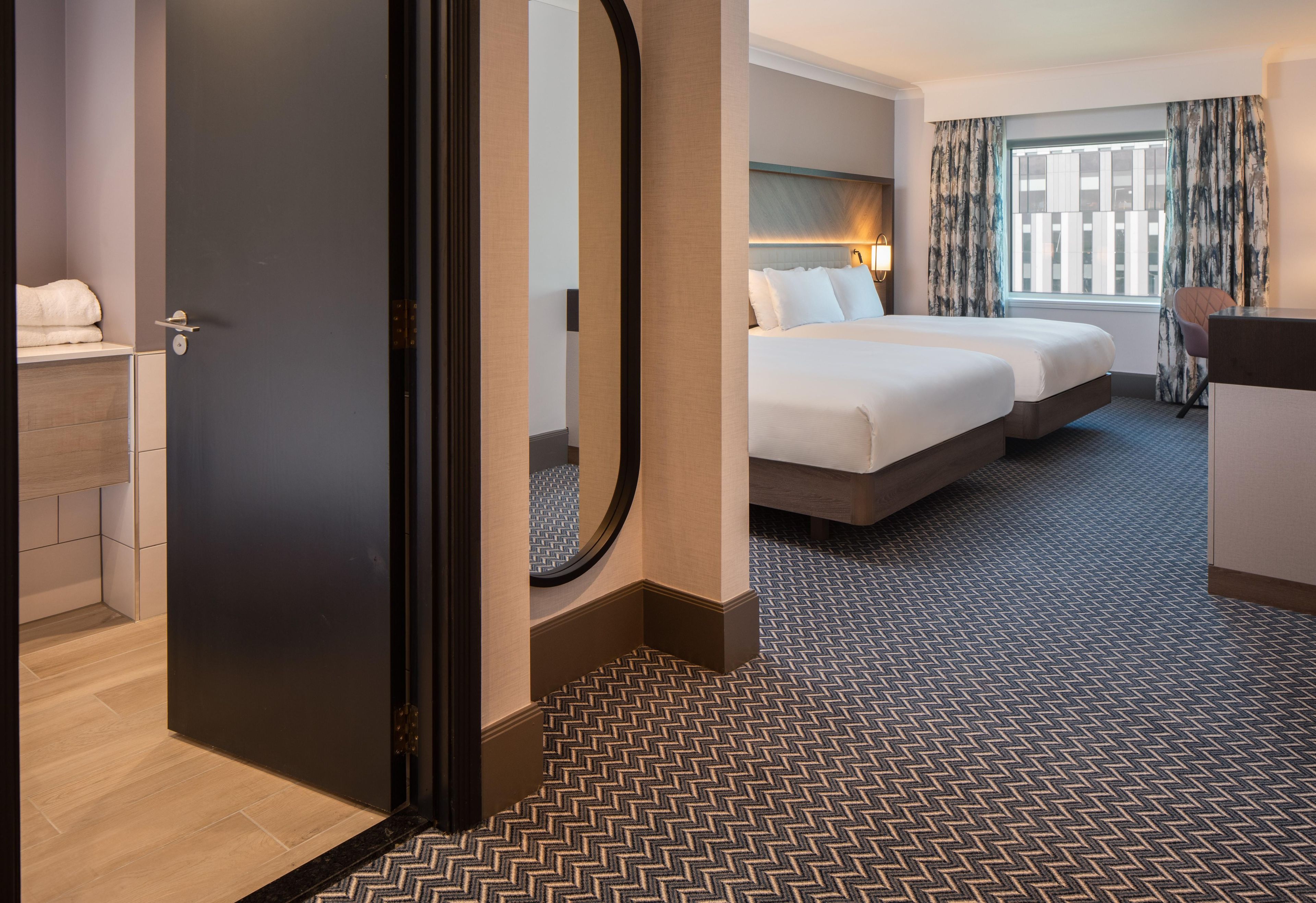 A hotel room with a large bed, a desk, a chair, and a bathroom.
