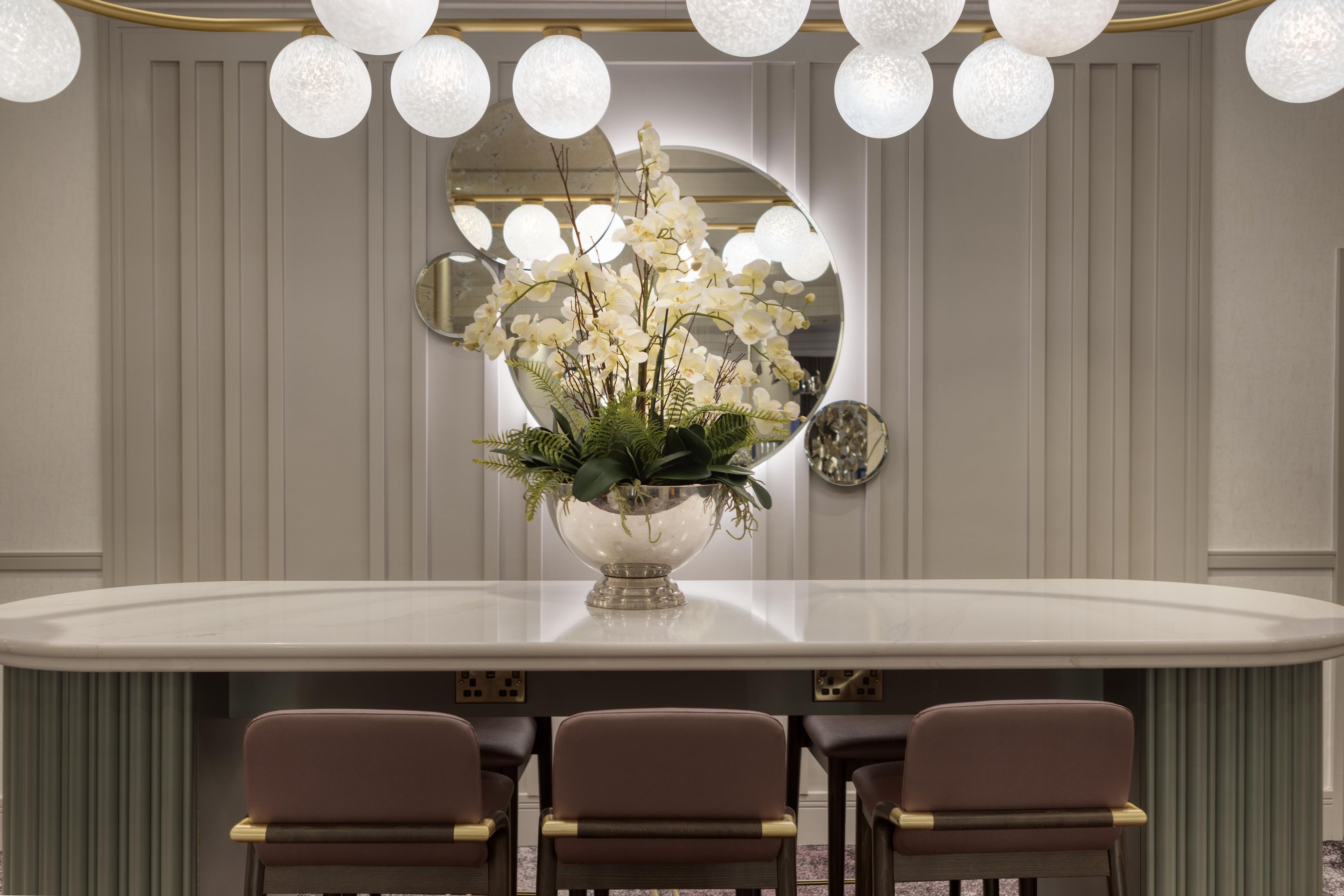 Une salle de conférence avec une table ronde, trois chaises et un arrangement floral au centre.