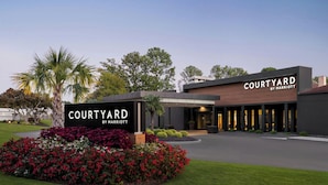 Eingang eines Courtyard by Marriott Hotels mit angelegtem Garten, moderner Architektur und blauem Himmel.