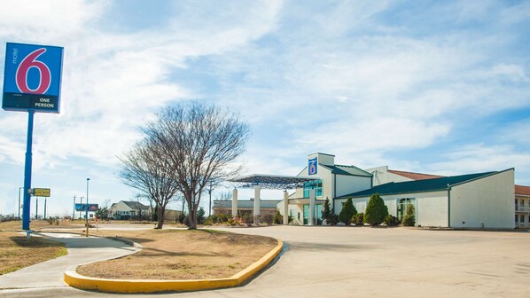 Welcome to the motel, featuring a modern design with a flat roof and large windows, set amidst a well-manicured lawn and parking area.