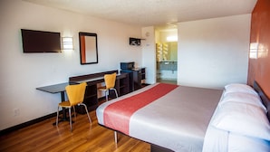 Hotelkamer met een bed, een bureau met stoel, een televisie en een badkamer die door een open deur zichtbaar is.