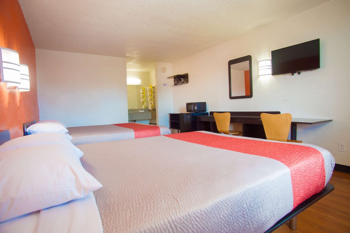 Une chambre d’hôtel avec deux lits, un bureau, une chaise, une télévision et un miroir.