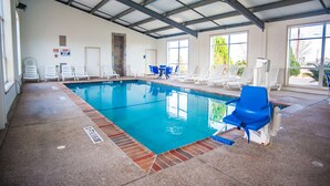 Una piscina interior con agua azul cristalina, rodeada de sillas blancas y azules para relajarse.