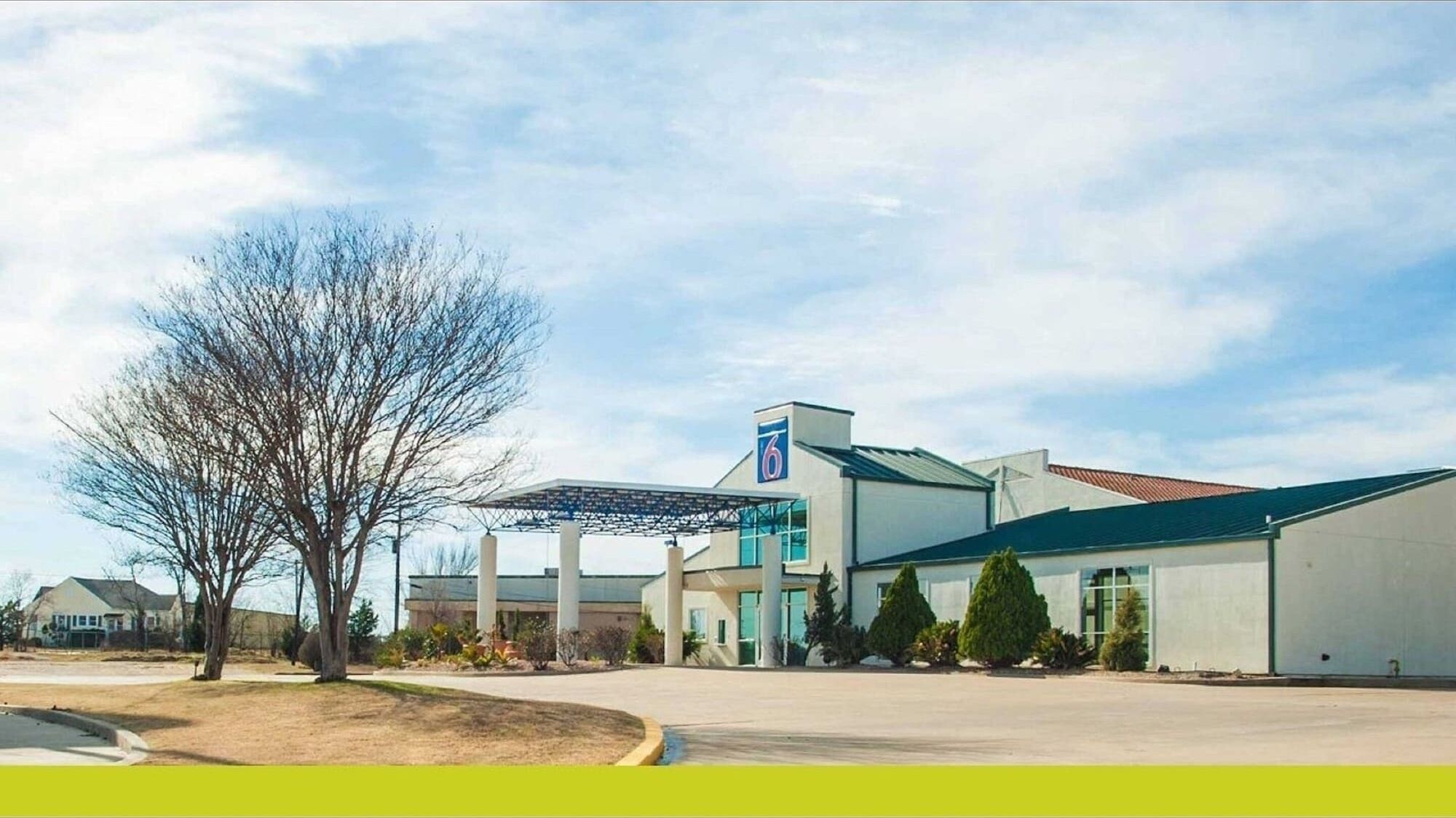 A modern hotel with a large parking lot, a covered outdoor area, and a prominent '6' logo on the building.