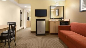 A hotel room with a kitchenette, a TV, a refrigerator, a sofa, and a dining area with chairs. - Travelodge Suites by Wyndham Moncton (Moncton)