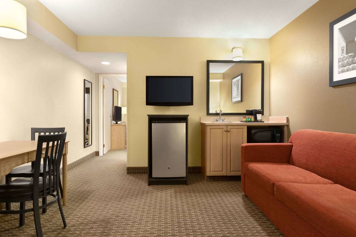 Quarto de hotel com cozinha compacta, televisão, frigorífico, sofá e área de jantar com cadeiras.