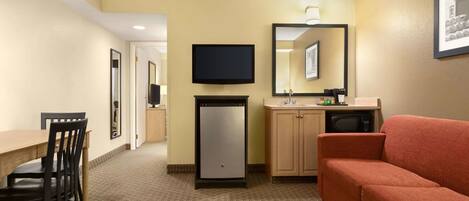 Habitación de hotel con kitchenette, televisor, refrigerador, sofá y comedor con sillas.