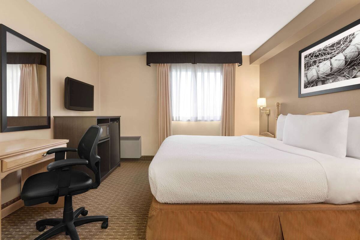 Quarto de hotel com cama, escrivaninha, cadeira, televisão e obras de arte na parede.