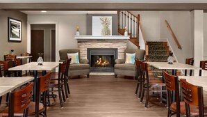 A dining area with a fireplace, wooden flooring, and a staircase. - Travelodge Suites by Wyndham Moncton (Moncton)