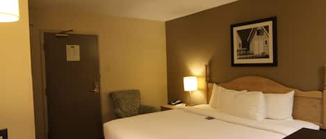 A hotel room with a large bed, a chair, a desk, a lamp, and a framed picture on the wall.