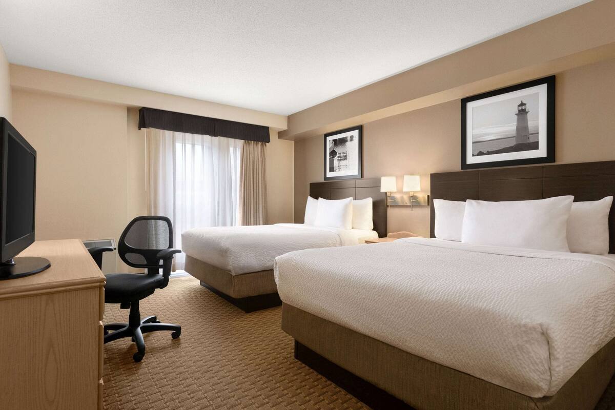 Quarto de hotel com duas camas, uma mesa com computador e televisão.