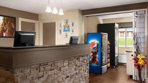 A reception area with a stone counter, a Pepsi refrigerator, and framed photos on the wall. - Travelodge Suites by Wyndham Moncton (Moncton)