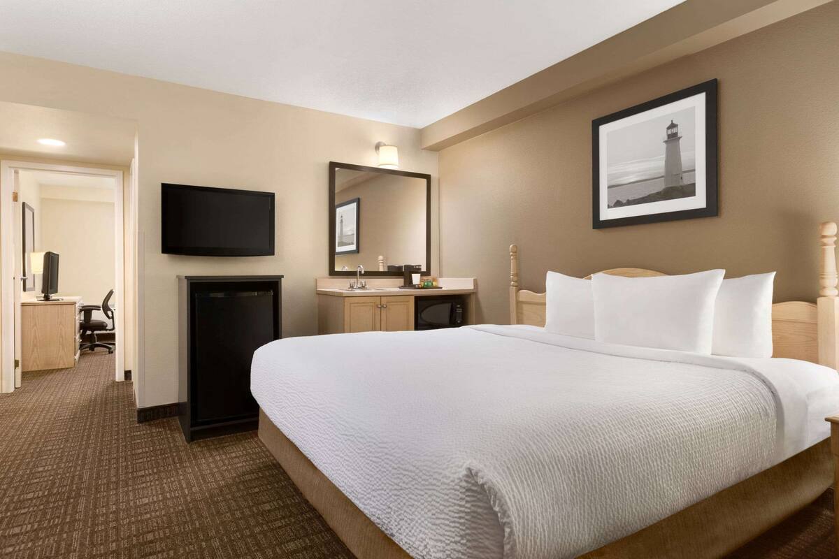 Quarto de hotel com uma cama grande, uma escrivaninha com computador, televisão e banheiro com pia e espelho.