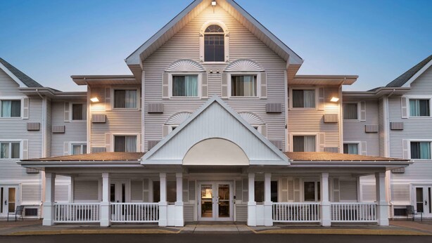 A large, multi-story hotel with a symmetrical facade, a central entrance with a semi-circular arch, and a covered front porch with white railings. - Travelodge Suites by Wyndham Moncton (Moncton)