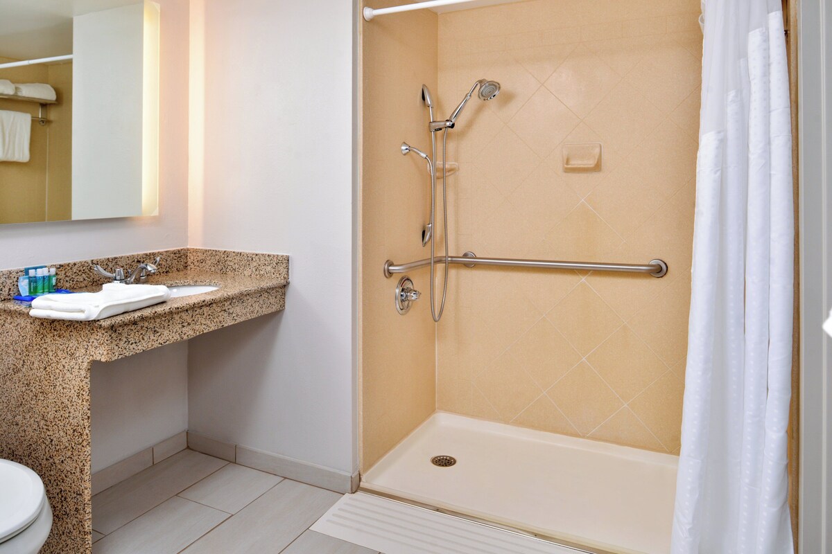 A bathroom with a shower, a sink, a toilet, and a mirror.