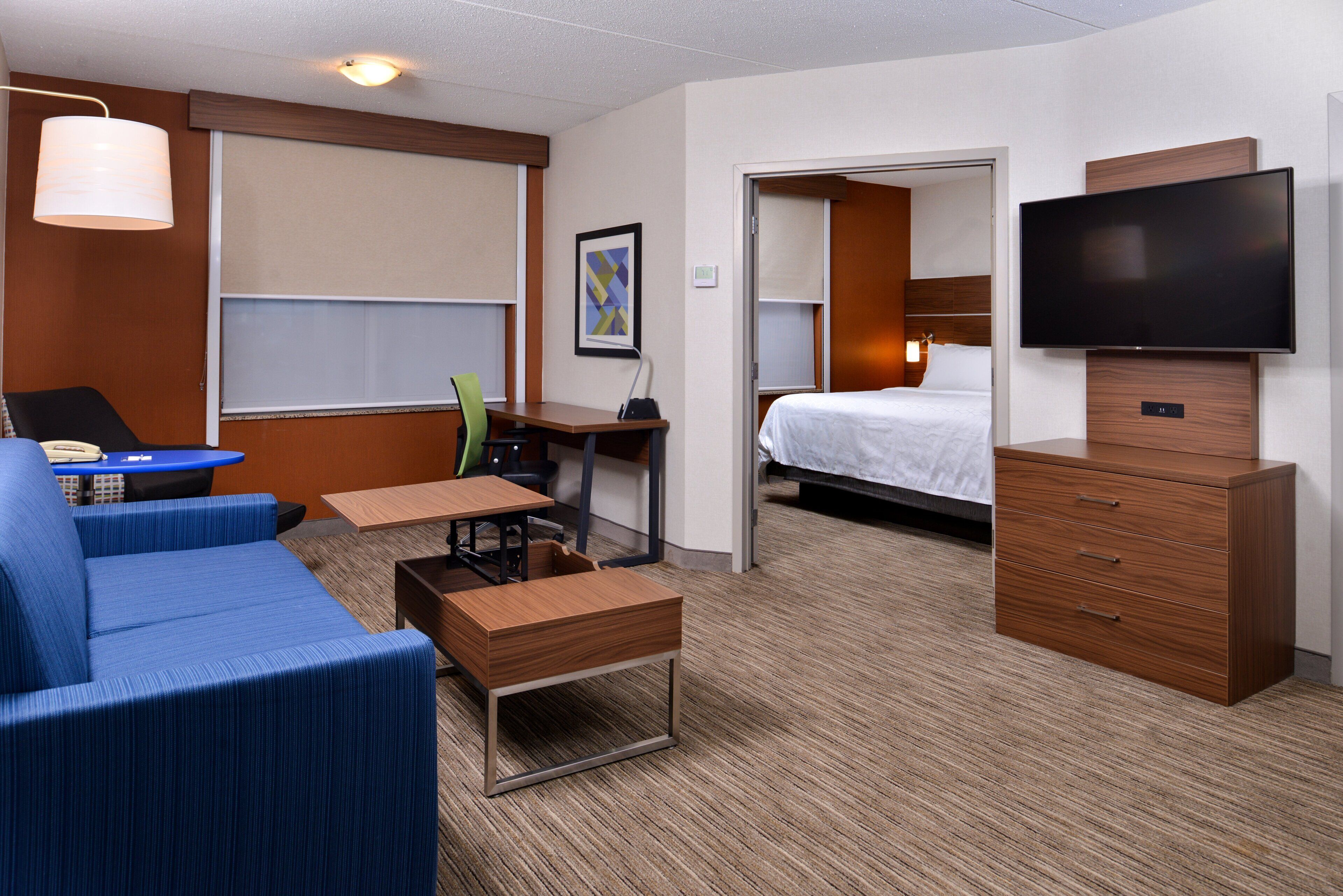 A hotel room with a bed, a desk, a chair, a TV, and a sofa.